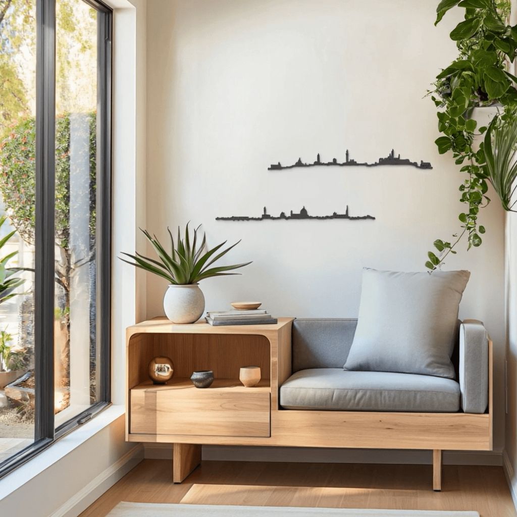 Rincón de lectura luminoso con asiento de madera y cojines gris suave, plantas verdes y skylines de madera de Florencia y Siena colgados en la pared.