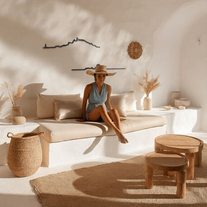 Skyline de Ibiza y Es Vedrà en madera negra decorando una pared encalada de estilo mediterráneo, con sofá de obra, cojines de lino y detalles rústicos en mimbre y madera natural.